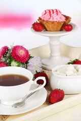 Cup of tea with cakes on wooden tray on table in room