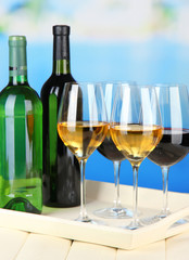 Wine bottles and glasses of wine on tray, on bright background