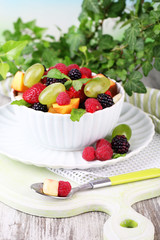 Fruit salad in bowl, on wooden table, on bright background