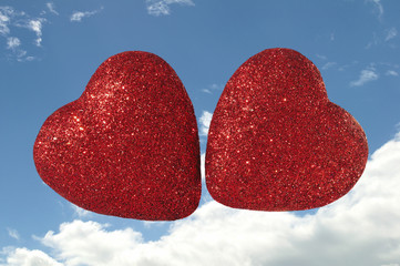 Two Glittery Red Hears Floating in Cloudy Blue Sky .