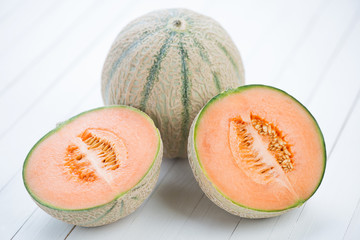 Whole and halved cantaloupe melons on white wooden background