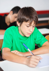 Teenage Schoolboy Writing At Desk During Examination