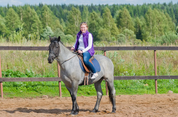Beautiful smiling girl riding a gray horse