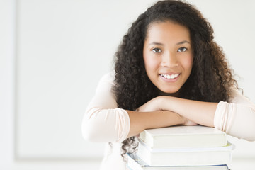 Girl Leaning On Stacked Books In Classroom