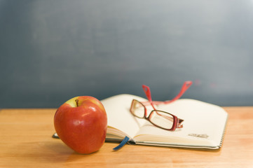 A book, glasses and apple on a desk in a school.