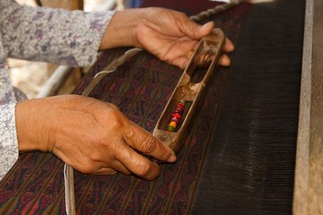 Woman working at Thai traditional loom with wooden bobbin