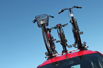 drei Fahrräder auf dem Dach eines roten Autos
