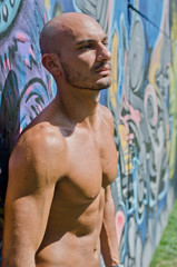 Handsome bald young man shirtless on graffiti wall