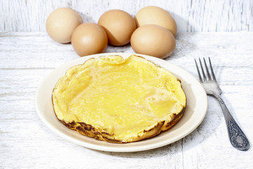 Omelette on wooden table. Basket with eggs in the background