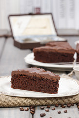 Chocolate cake on white plate, on hessian. Coffee beans on wood