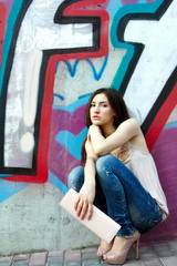 Fototapeta na wymiar Outdoors portrait of beautiful fashion girl sitting near wall wi