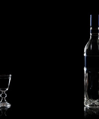 Bottle and glass of vodka on black background
