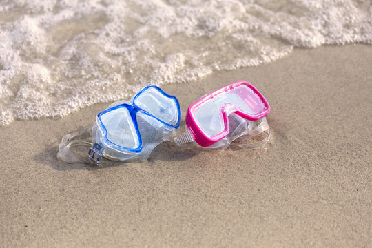 Summer time: Red and blue gogles on the sand washed by the ocean