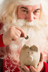 Authentic Santa Claus holding piggy bank and putting golden coin