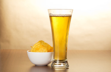 Glass of light beer and bowl with chips against paper