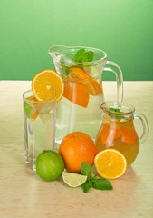 Jugs with drinks, a glass, a juicy lime and oranges