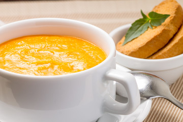 Pumpkin soup in white bowl with fresh basil