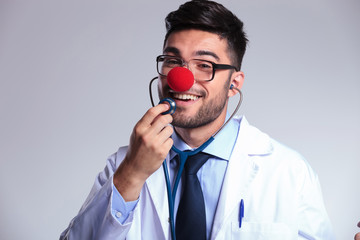 young doctor with clown red nose listens to himself