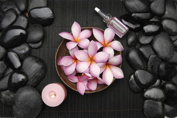 frangipani flower in bowl with candle and oil and pile stones