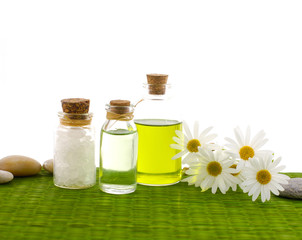 spa oil with salt in glass bottle, daisy flowers, stones on mat