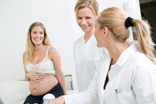 Doctors Looking At Each Other With Pregnant Woman In Clinic