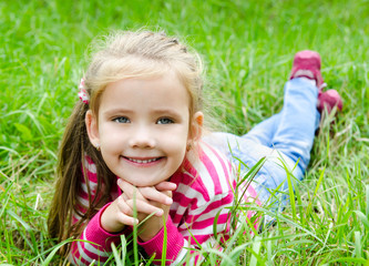 Cute smiling little girl lying in grass on the meadow