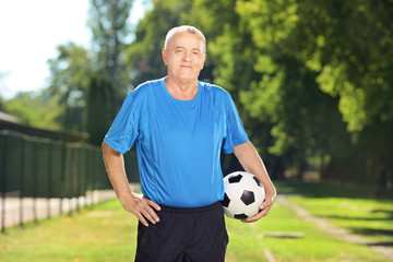 Mature man in sportswear holding a ball in a park