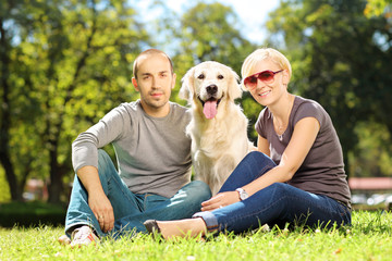 Smiling young couple hugging a dog in a park