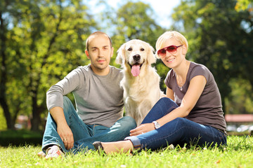Fototapeta premium Smiling young couple hugging a dog in a park