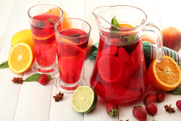 sangria in jar and glasses with fruits, on white wooden table