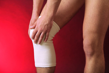 Young man with elastic bandage on knee, on red background
