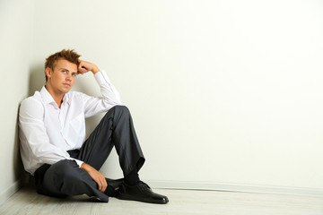 Young businessman  sitting on floor, on gray wall background