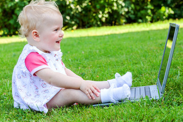 Baby sitting with laptop in a meadow