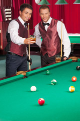 Pool game. Two cheerful young men playing pool and drinking