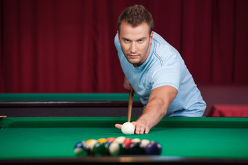 Man playing pool. Confident young man playing pool and looking c