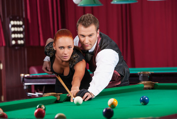 Playing pool. Confident man teaching beautiful young woman to pl