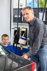 Mature man with son refueling vehicle with gasoline