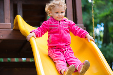 Curly blonde girl sliding at playground