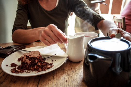 Young woman pouring herself a cup of tea and eating cake in cafe