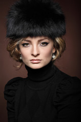 Portrait of beautiful blonde in a fur cap on a brown 