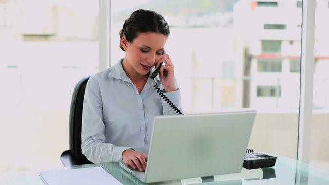 Happy businesswoman typing and talking on the phone