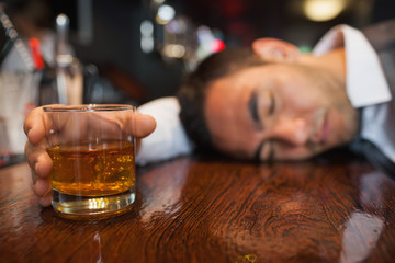 Drunk businessman with whiskey in his hand lying on a counter