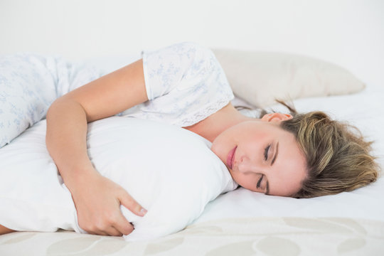 Peaceful woman lying on bed embracing pillow