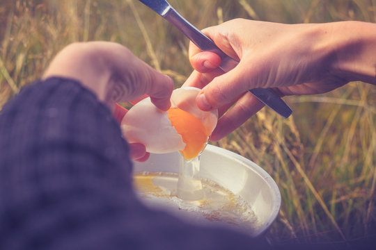 Woman cracking an egg on portable camping stove