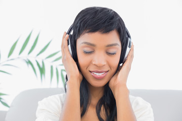 Fototapeta premium Dreamy black haired woman in white clothes listening to music