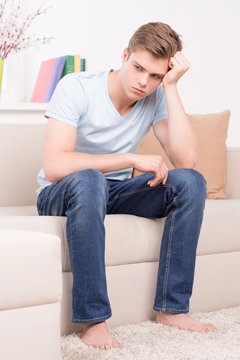 Depressed man. Sad young man sitting on the couch and holding ha