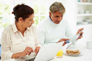 Fototapeta na wymiar Senior Indian Couple Using Laptop And Digital Tablet At Home