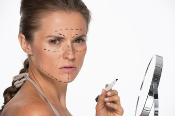 Woman with plastic surgery marks on face holding mirror 