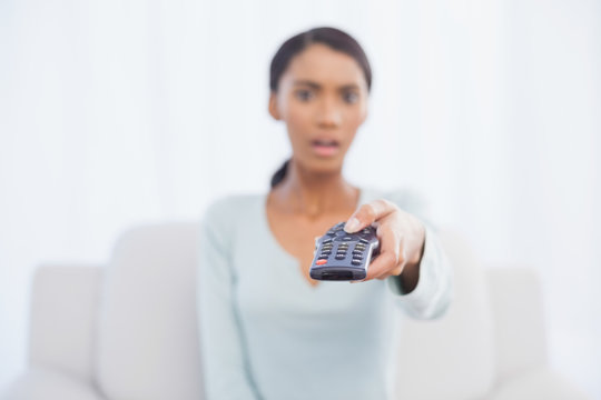 Shocked woman sitting on sofa changing tv channel