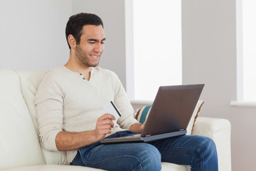 Cheerful handsome man using his credit card to buy online
